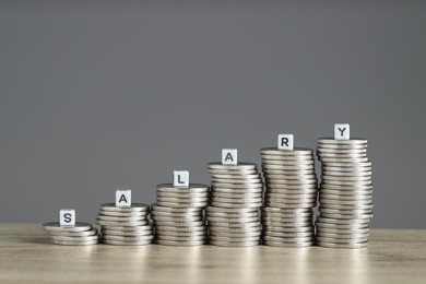 Photo of Word Salary made of cubes and stacked coins on wooden table against grey background