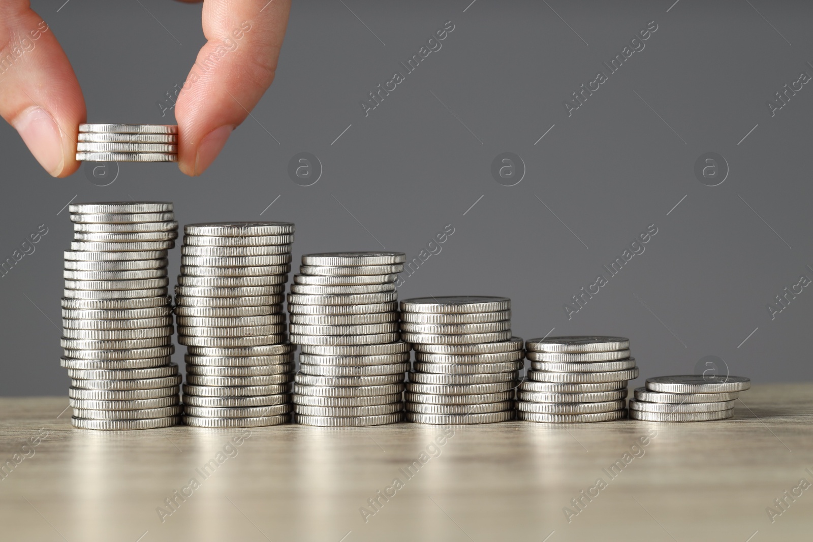 Photo of Woman putting coins at wooden table against grey background, closeup. Salary concept