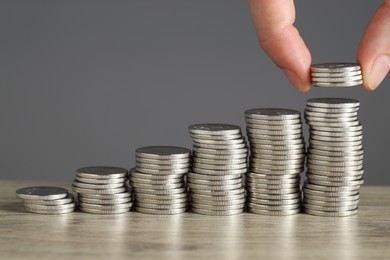 Photo of Woman putting coins at wooden table against grey background, closeup. Salary concept