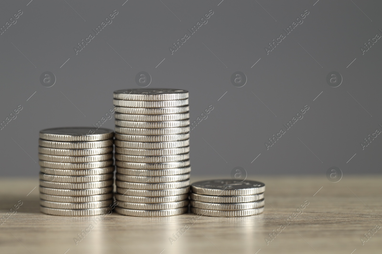 Photo of Stacked coins on wooden table against grey background, closeup with space for text. Salary concept