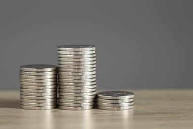 Photo of Stacked coins on wooden table against grey background, closeup with space for text. Salary concept