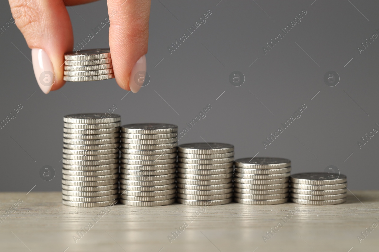 Photo of Woman putting coins at wooden table against grey background, closeup. Salary concept