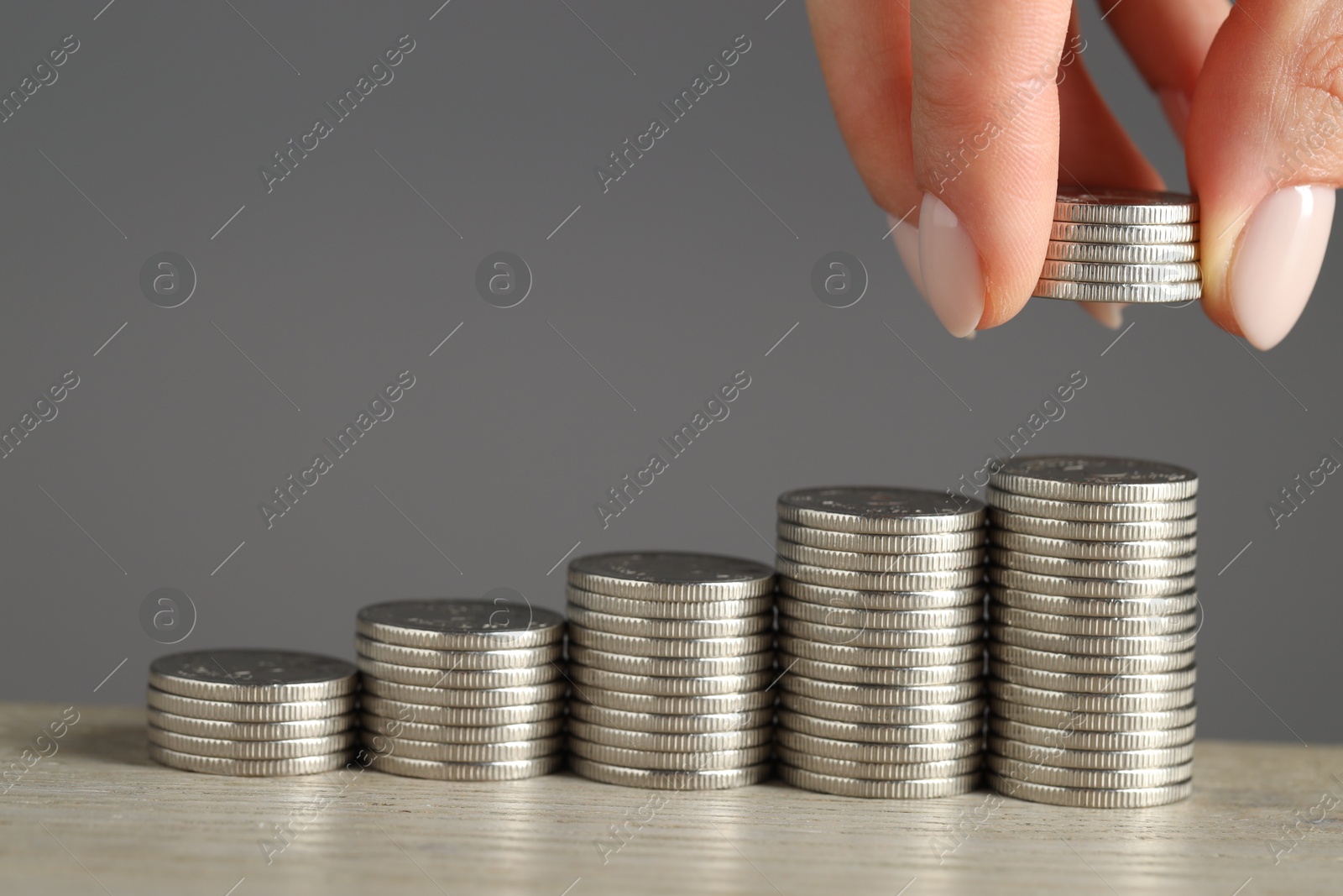 Photo of Woman putting coins at wooden table against grey background, closeup. Salary concept