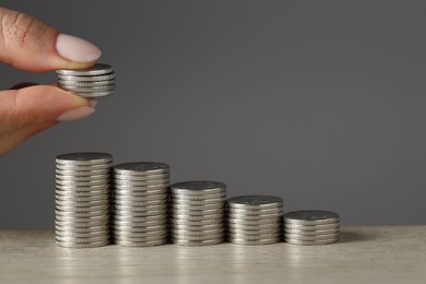 Photo of Woman putting coins at wooden table against grey background, closeup. Salary concept