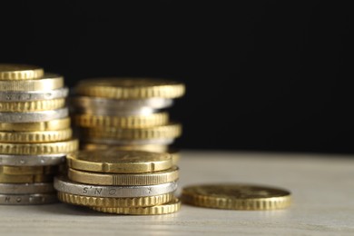 Photo of Stacked coins on wooden table against black background, closeup with space for text. Salary concept