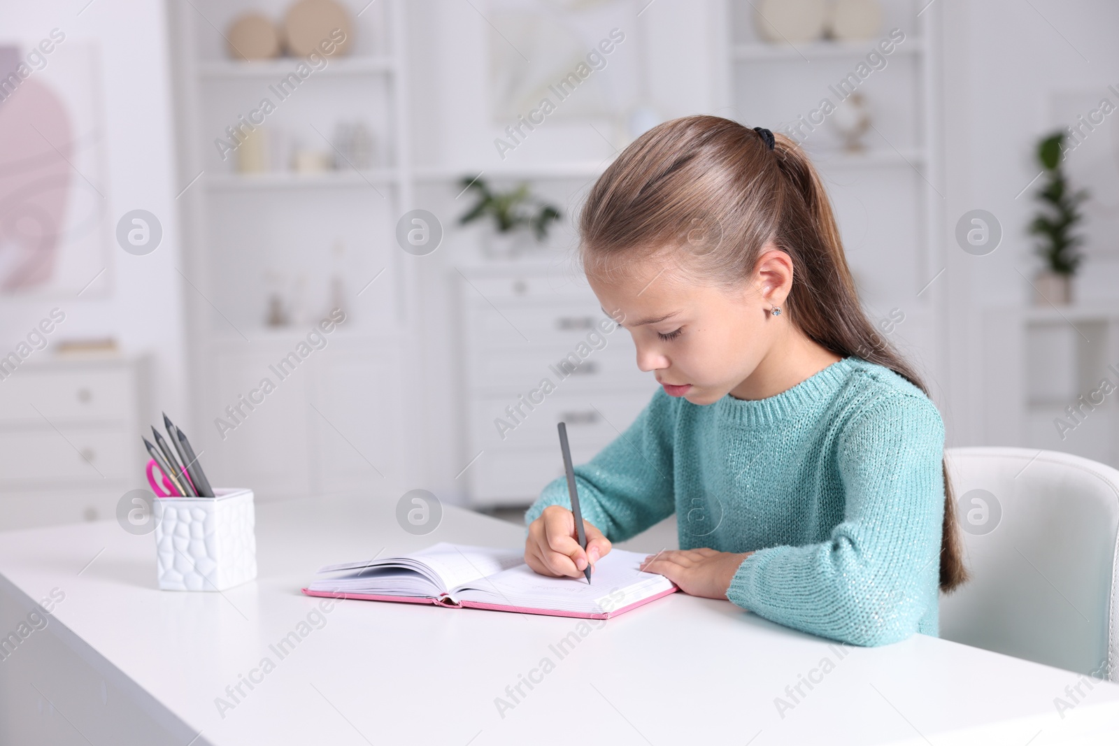 Photo of Girl with correct posture doing homework at white desk indoors