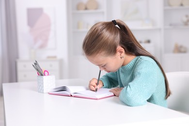 Photo of Girl with incorrect posture doing homework at white desk indoors