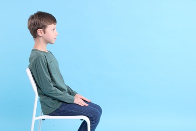 Boy with correct posture sitting on chair against light blue background