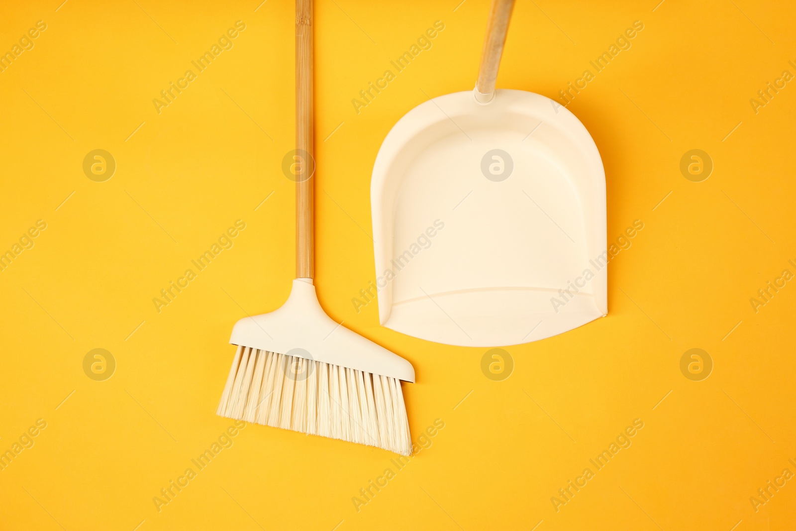 Photo of Cleaning broom and dustpan on orange background, flat lay