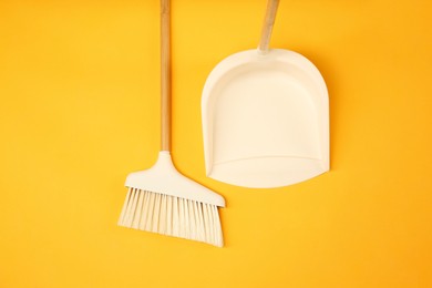 Photo of Cleaning broom and dustpan on orange background, flat lay