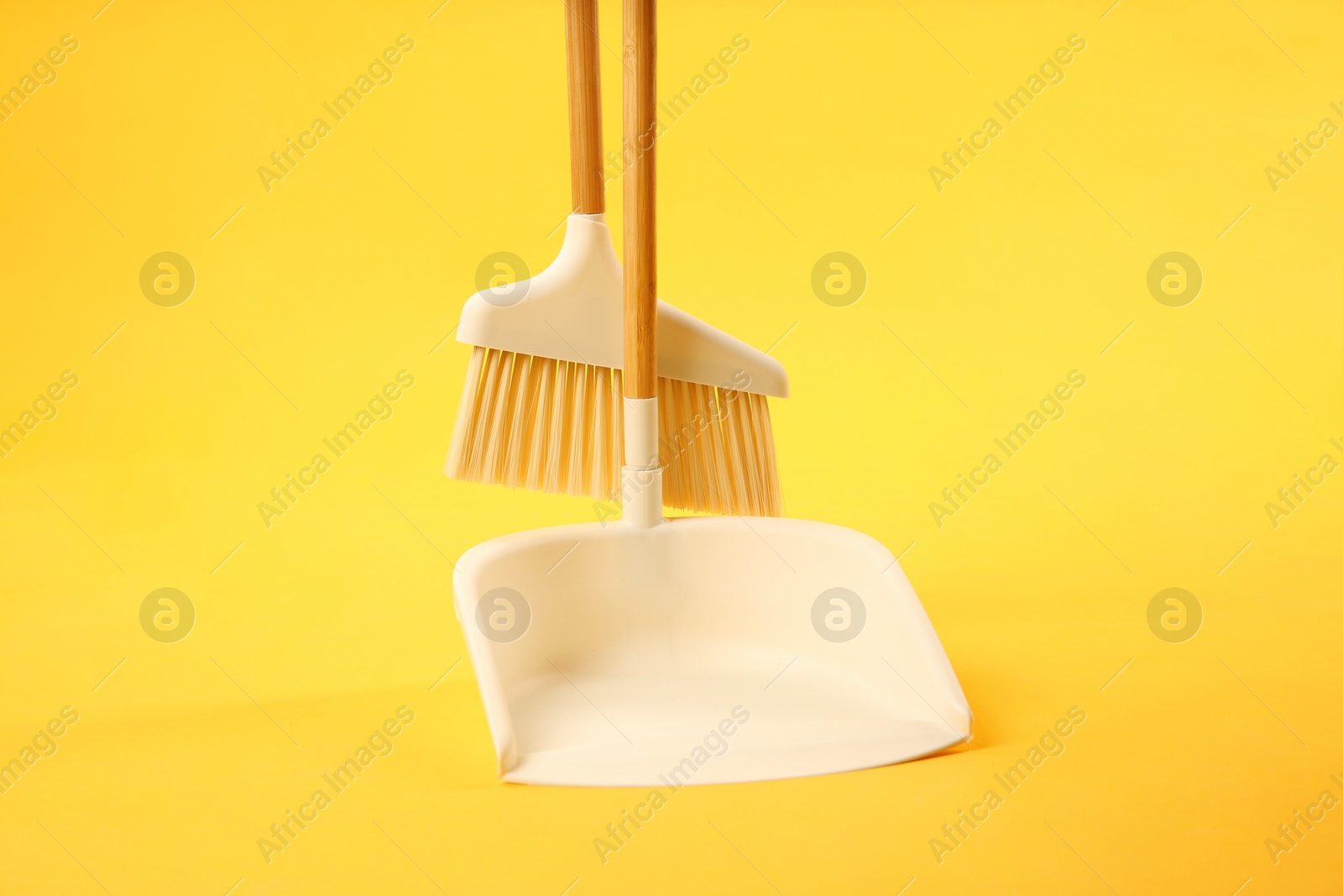 Photo of Cleaning broom and dustpan on yellow background