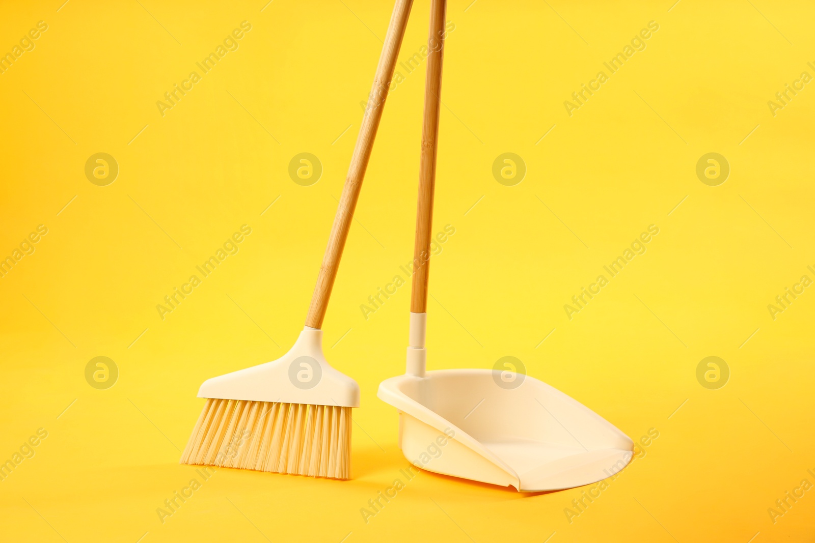 Photo of Cleaning broom and dustpan on yellow background