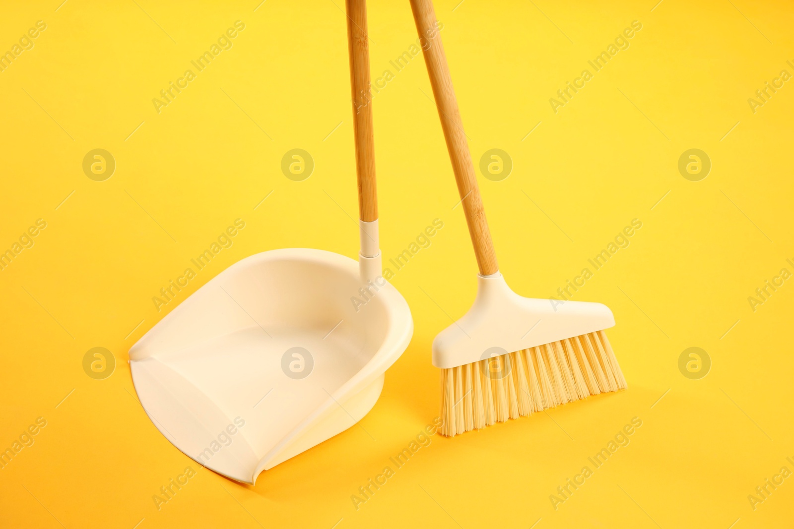 Photo of Cleaning broom and dustpan on yellow background