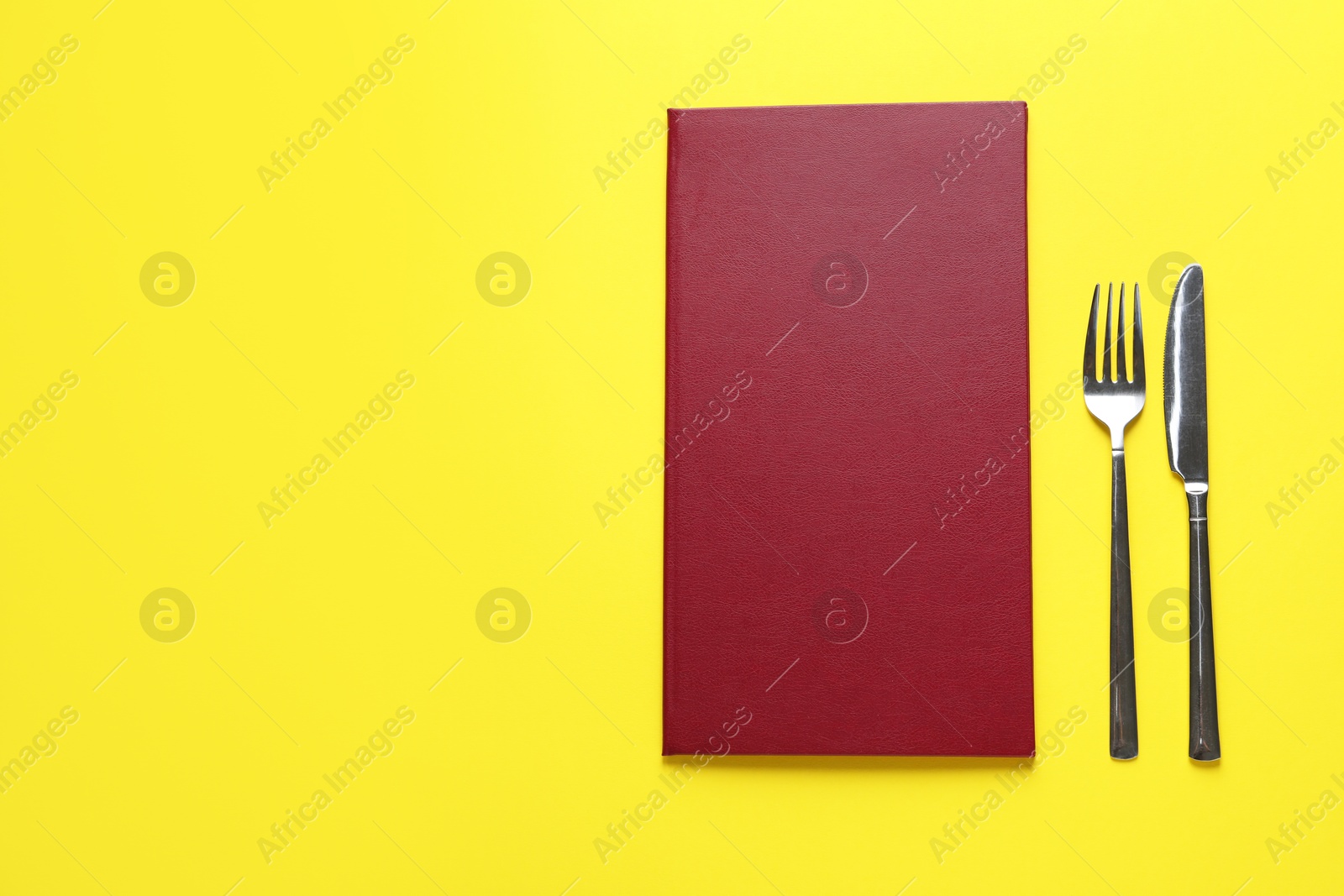 Photo of Hardcover menu and cutlery on yellow table, flat lay. Space for text