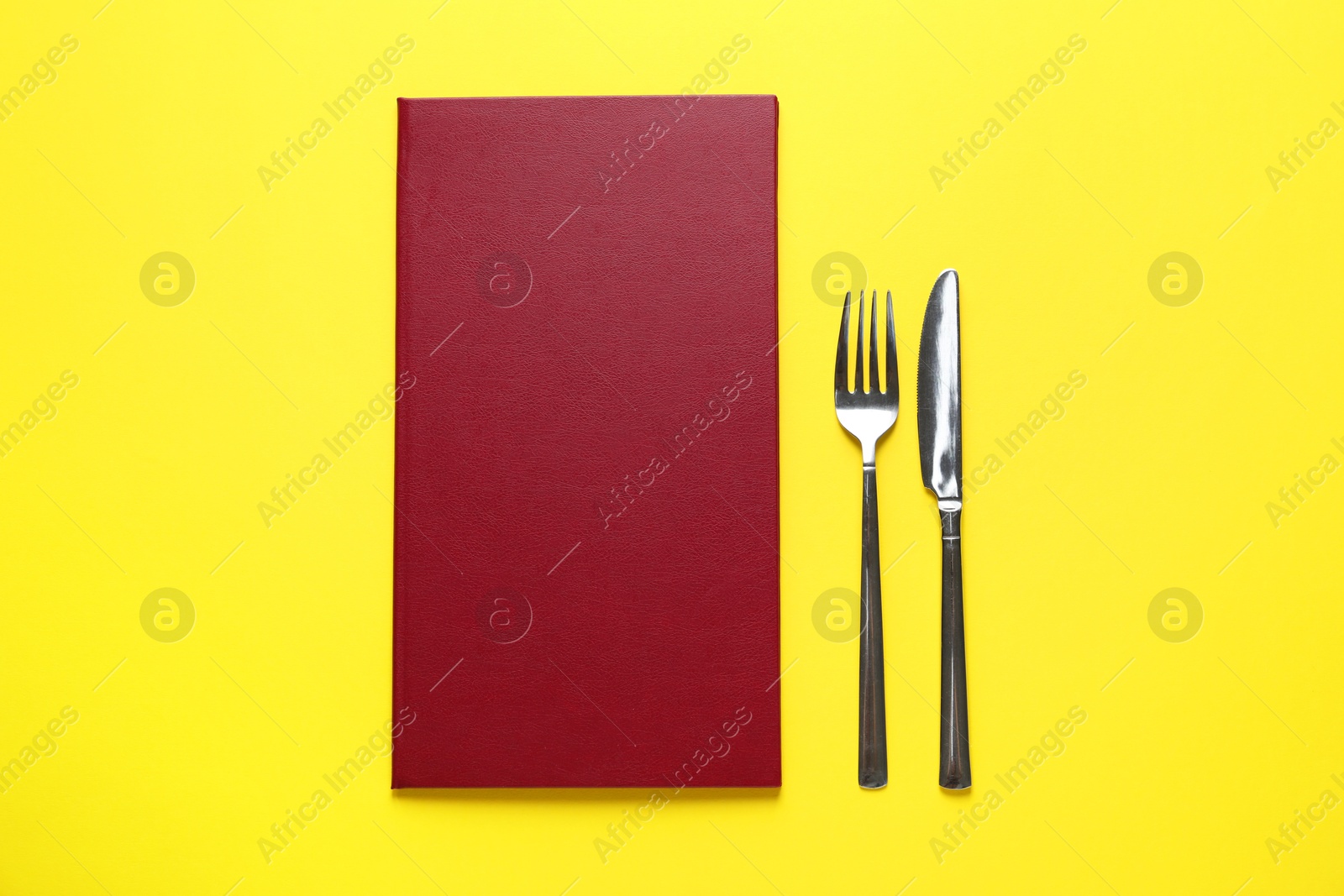 Photo of Hardcover menu and cutlery on yellow table, flat lay