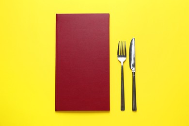 Photo of Hardcover menu and cutlery on yellow table, flat lay