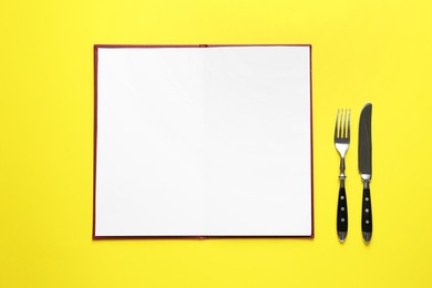 Photo of Hardcover notebook with blank sheets for menu design and cutlery on yellow table, flat lay