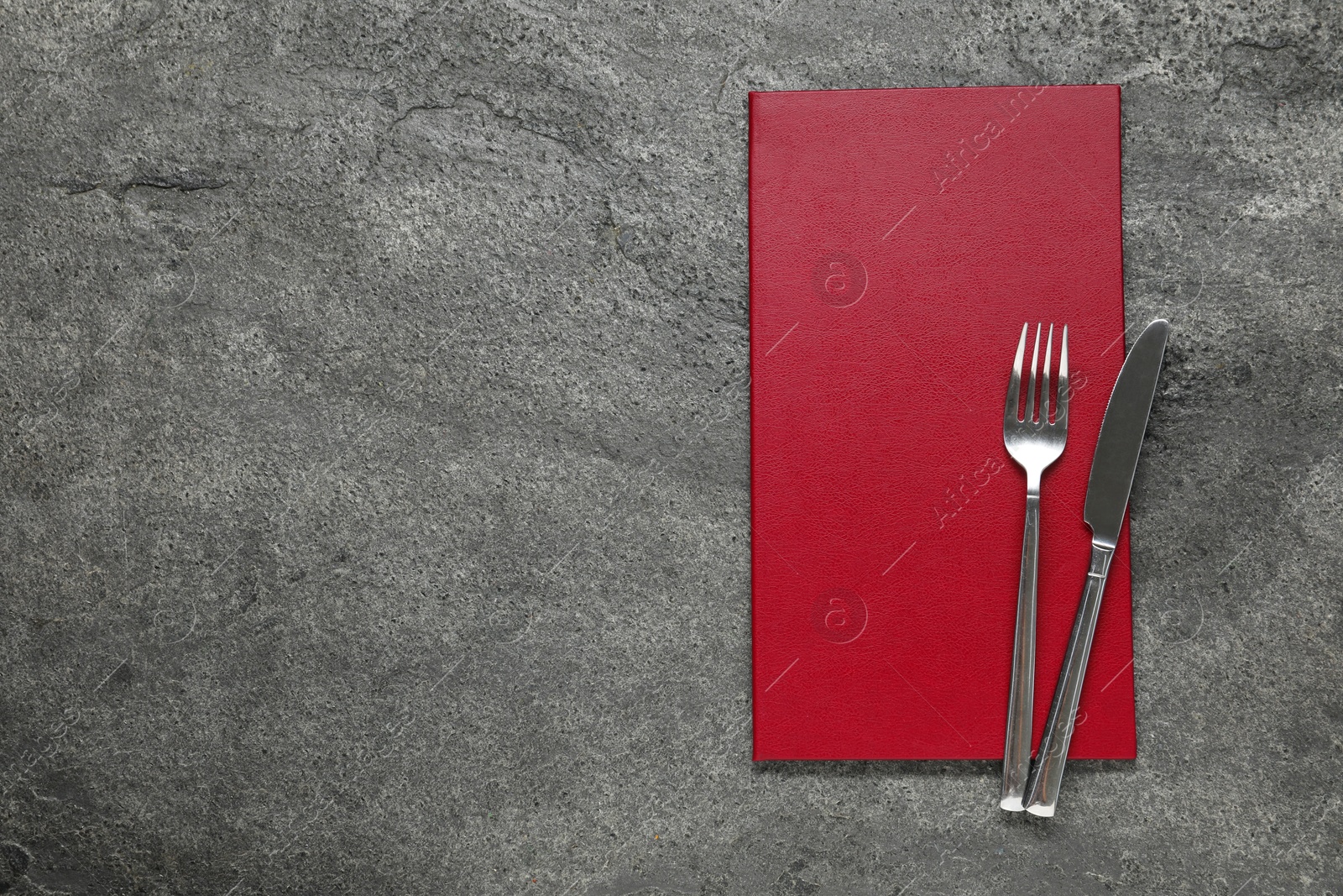 Photo of Hardcover menu and cutlery on grey textured table, top view. Space for text