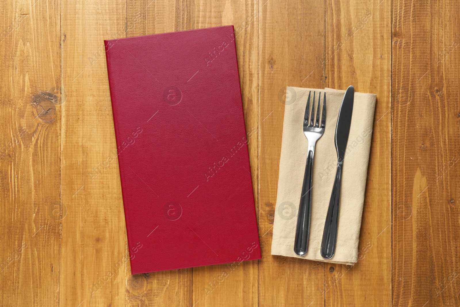 Photo of Hardcover menu and cutlery on wooden table, flat lay