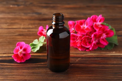 Photo of Geranium essential oil in bottle and beautiful flowers on wooden table