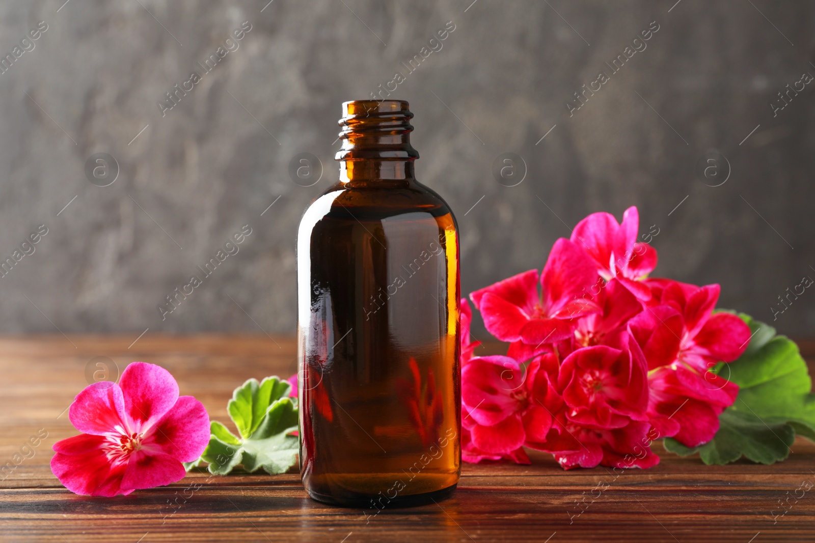 Photo of Geranium essential oil in bottle and beautiful flowers on wooden table