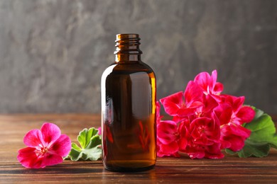 Photo of Geranium essential oil in bottle and beautiful flowers on wooden table