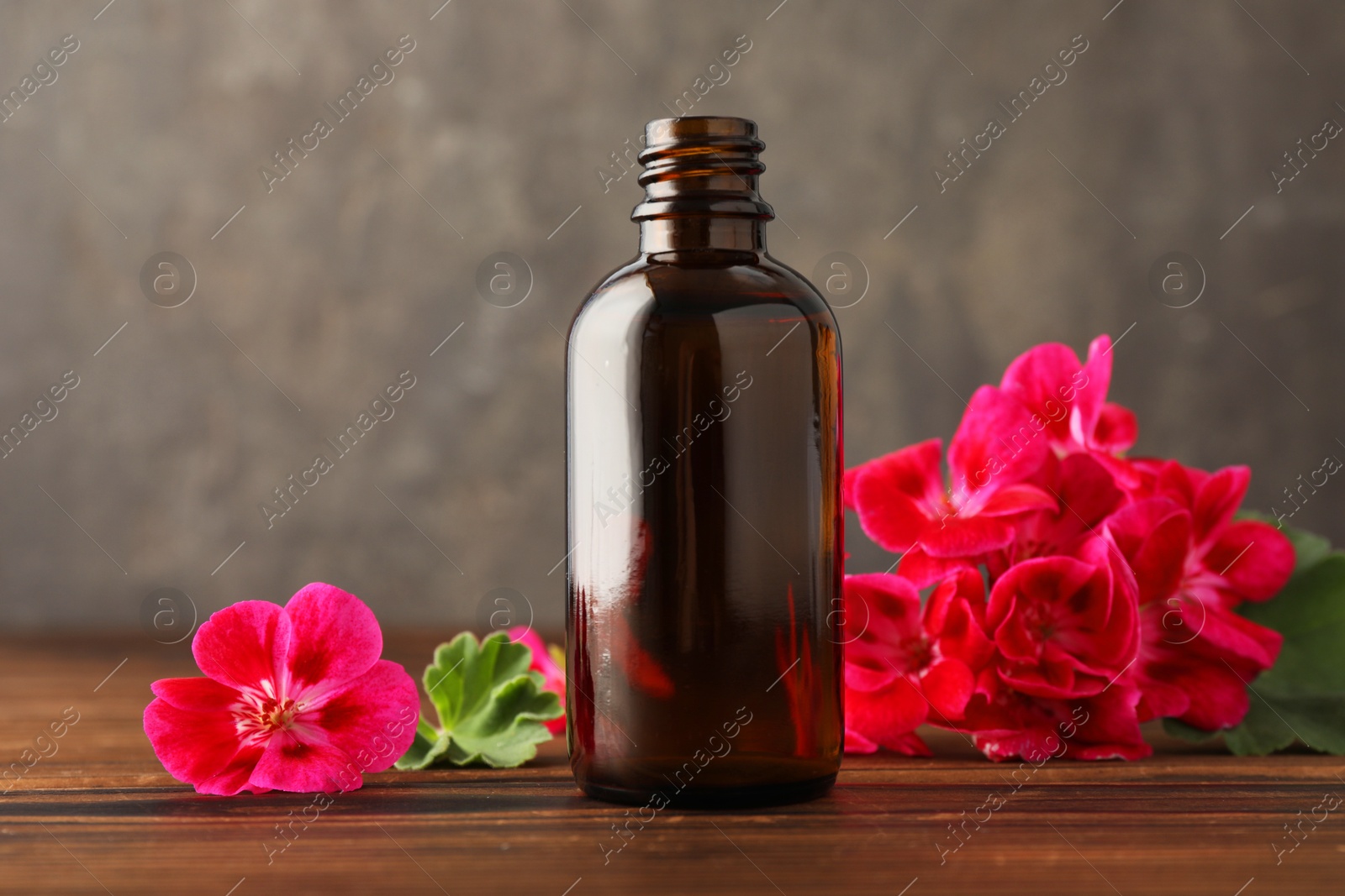 Photo of Geranium essential oil in bottle and beautiful flowers on wooden table