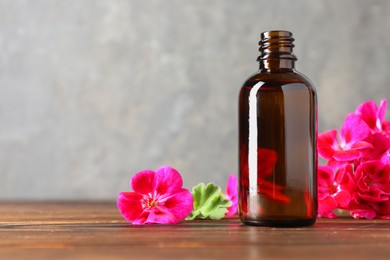 Photo of Geranium essential oil in bottle and beautiful flowers on wooden table, space for text