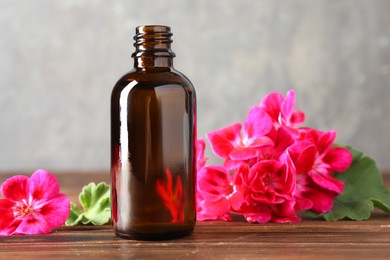 Photo of Geranium essential oil in bottle and beautiful flowers on wooden table