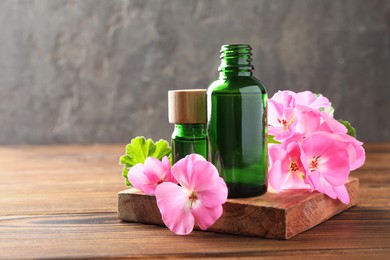 Geranium essential oil in bottles and beautiful flowers on wooden table, space for text