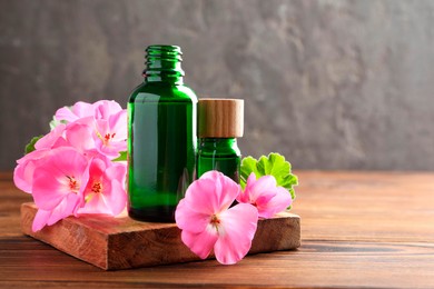 Photo of Geranium essential oil in bottles and beautiful flowers on wooden table, space for text