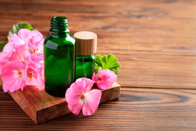 Photo of Geranium essential oil in bottles and beautiful flowers on wooden table, space for text