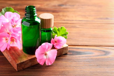 Photo of Geranium essential oil in bottles and beautiful flowers on wooden table, space for text