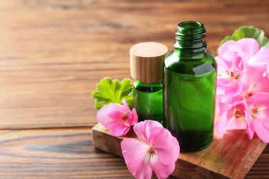 Photo of Geranium essential oil in bottles and beautiful flowers on wooden table, space for text