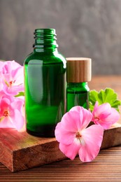 Geranium essential oil in bottles and beautiful flowers on wooden table