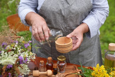 Photo of Senior woman making tincture at table outdoors, closeup