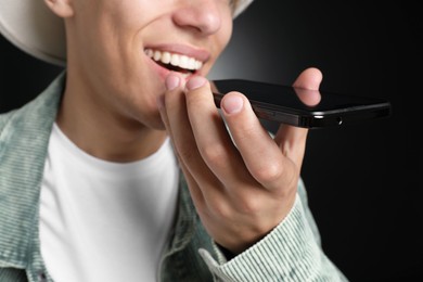 Photo of Young man recording voice message via smartphone on dark background, closeup