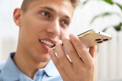 Young man recording voice message via smartphone at home, selective focus