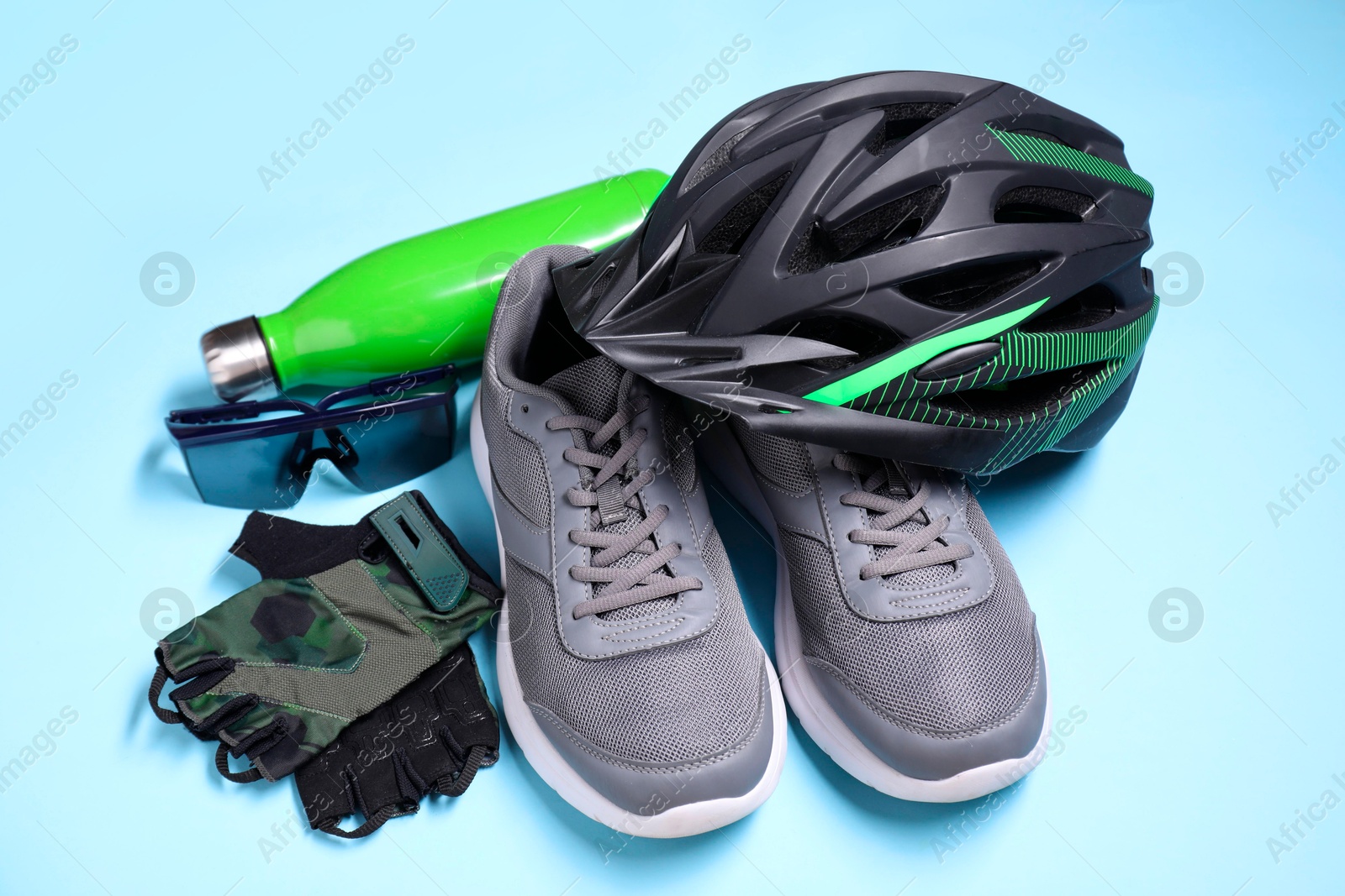 Photo of Bicycle helmet, sneakers, thermo bottle, fingerless gloves and goggles on light blue background