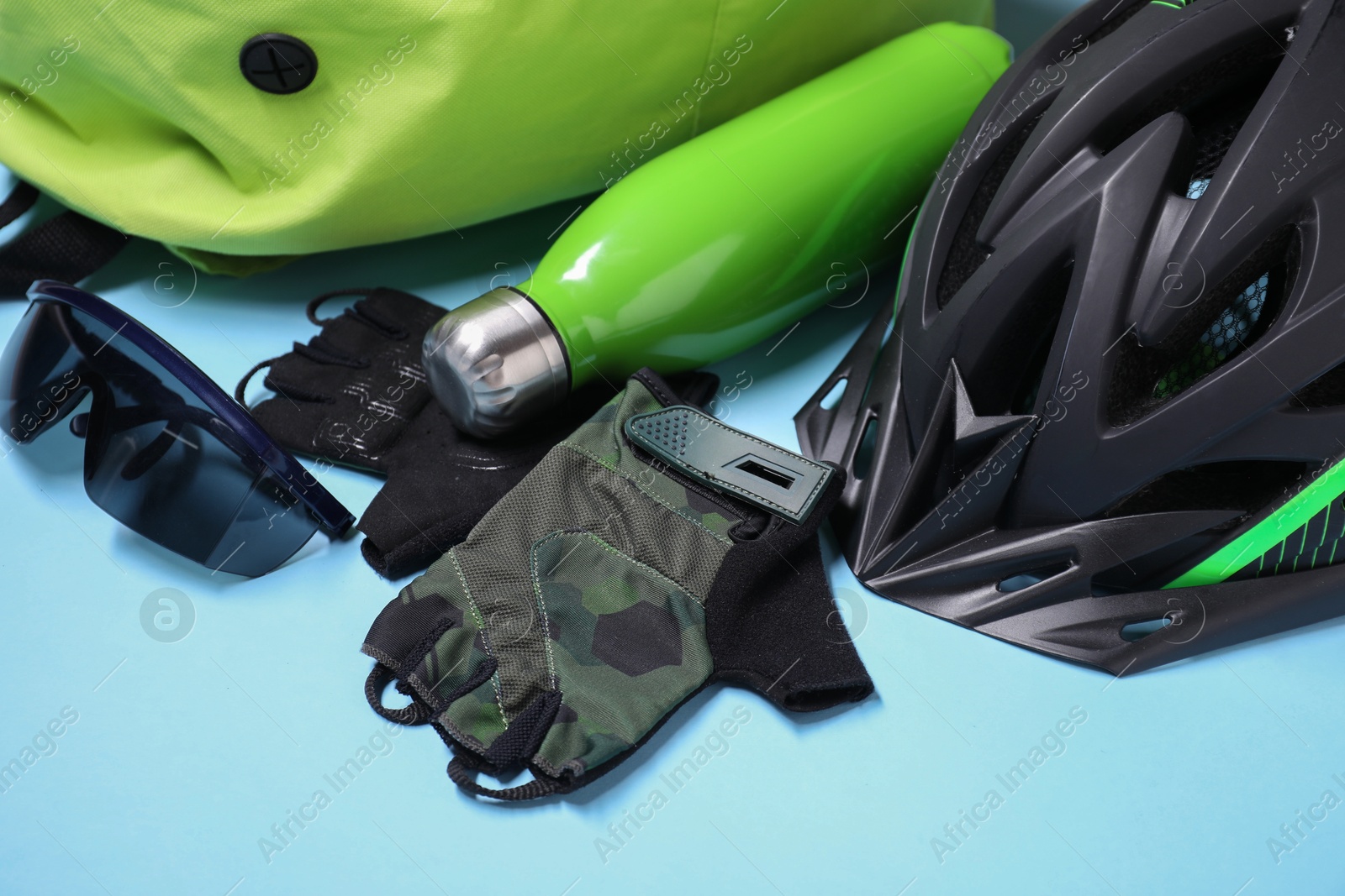 Photo of Bicycle helmet, thermo bottle, fingerless gloves and goggles on light blue background, closeup