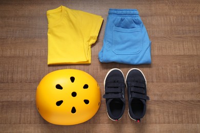 Photo of Bicycle helmet, sneakers and sportswear on wooden background, flat lay