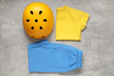 Bicycle helmet and sportswear on light gray textured background, flat lay