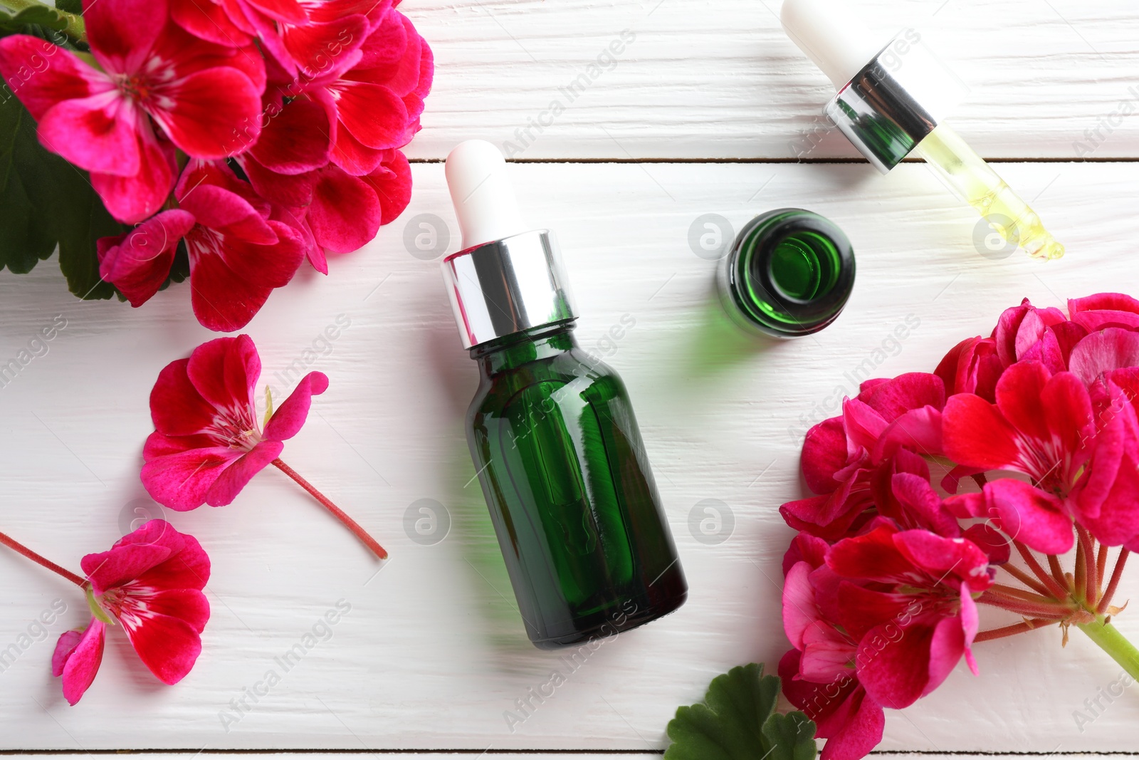 Photo of Geranium essential oil, pipette and beautiful flowers on white wooden table, flat lay