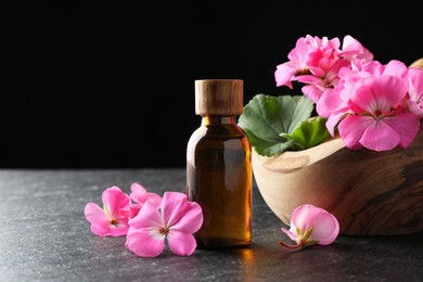 Photo of Bottle of geranium essential oil and beautiful flowers on black table, closeup