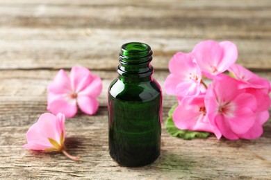 Photo of Bottle of geranium essential oil and beautiful flowers on wooden table, closeup