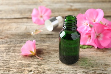 Geranium essential oil in bottle, pipette and beautiful flowers on wooden table, closeup