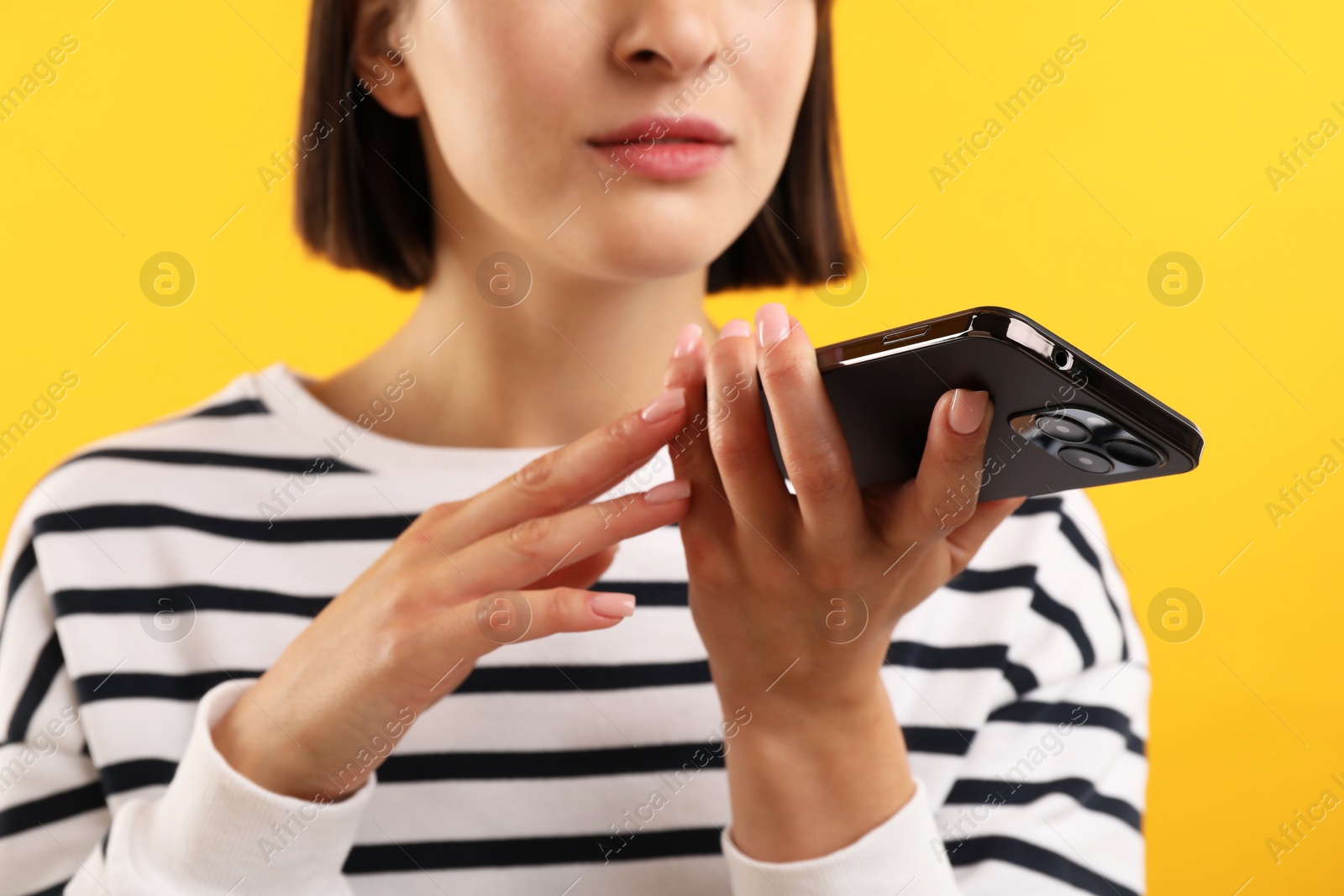 Photo of Woman recording voice message via smartphone on yellow background, closeup