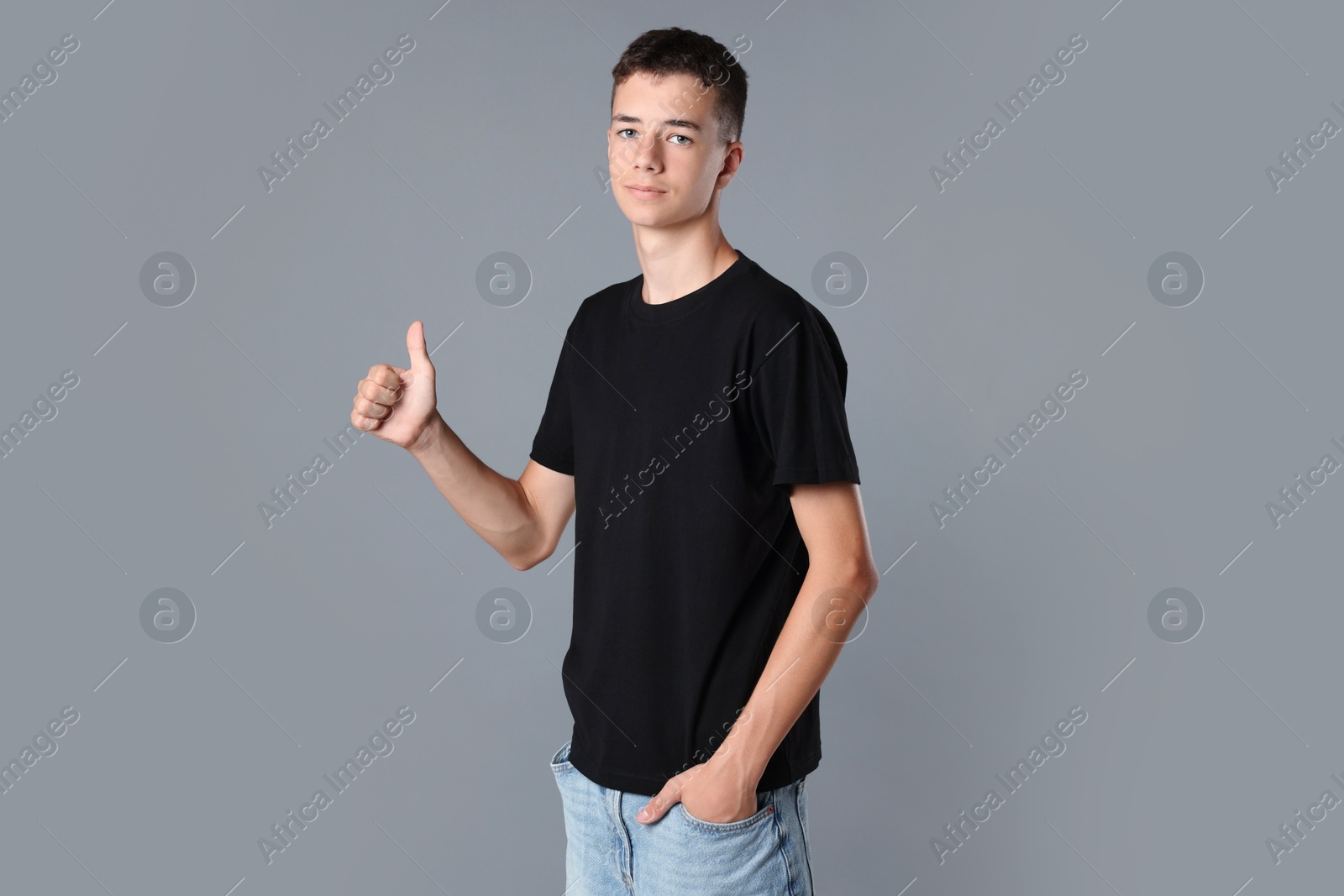 Photo of Teenage boy wearing black t-shirt and showing thumbs up on grey background