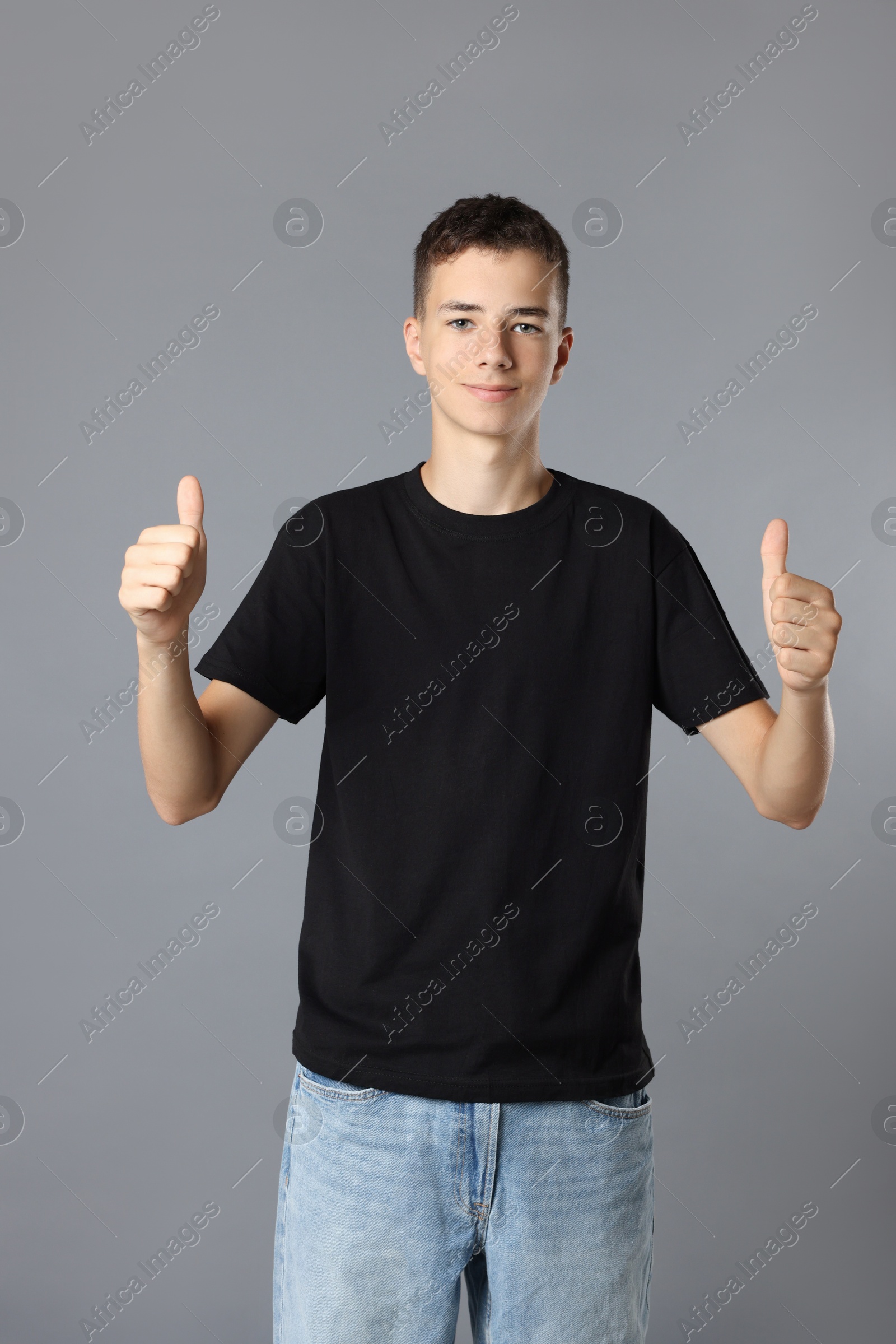 Photo of Teenage boy wearing black t-shirt and showing thumbs up on grey background