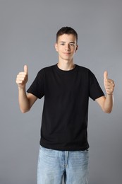 Photo of Teenage boy wearing black t-shirt and showing thumbs up on grey background